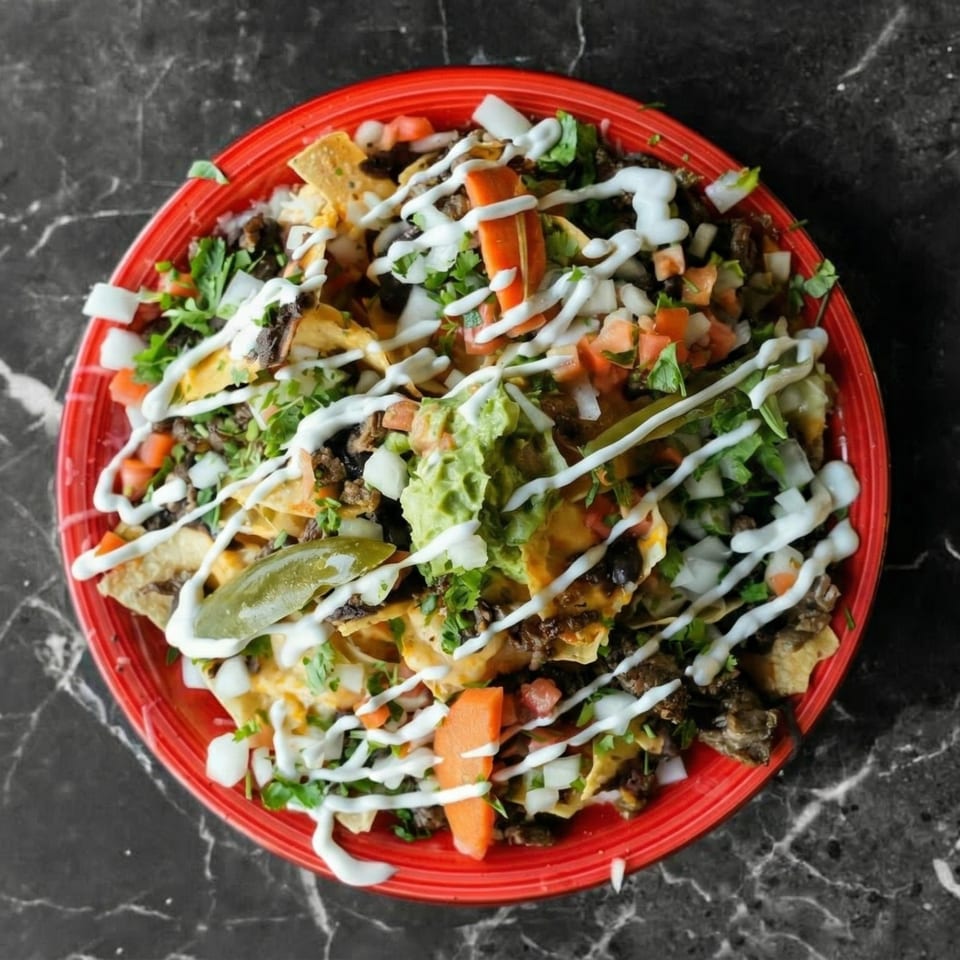 A vibrant red plate of loaded nachos with meat, cheese, guacamole, salsa, and sour cream.