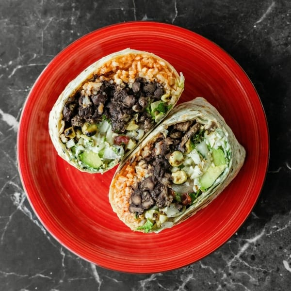 Two halves of a burrito filled with rice, black beans, avocado, and other ingredients on a red plate.