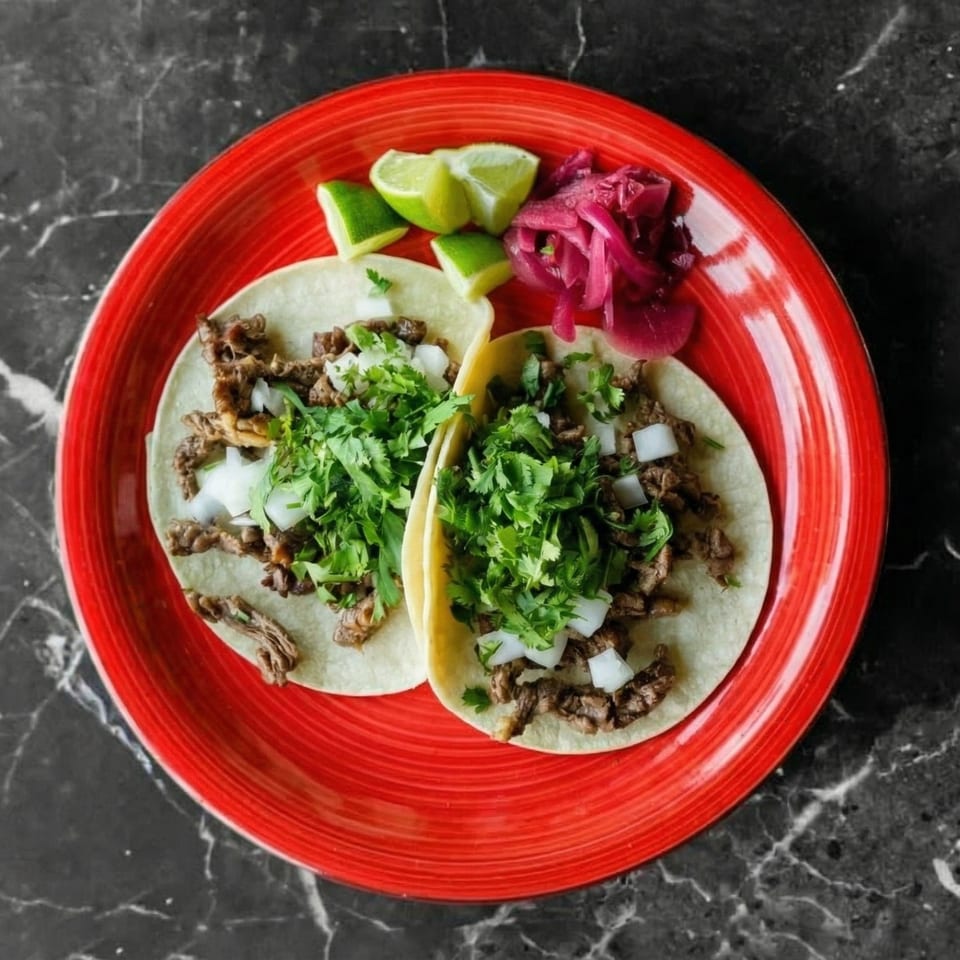 Two carne asada street tacos with cilantro, onions, lime, and pickled red onions on a red plate.