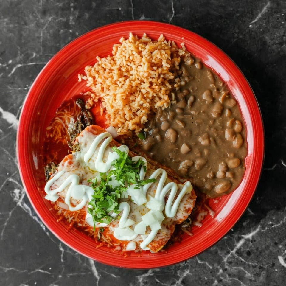 Red plate with enchiladas topped with sour cream, cilantro, and onions, alongside rice and beans.