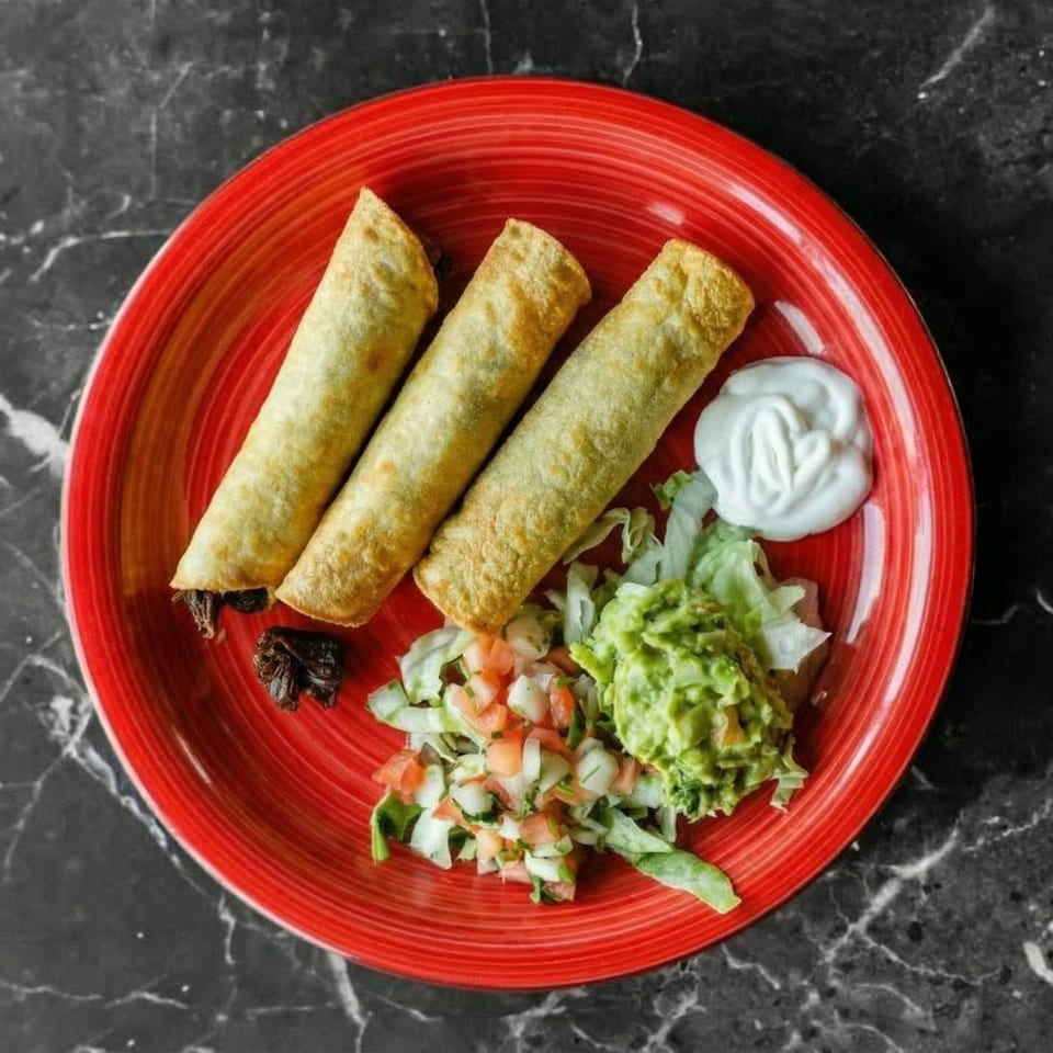 Three golden taquitos with guacamole, pico de gallo, and sour cream on a red plate.