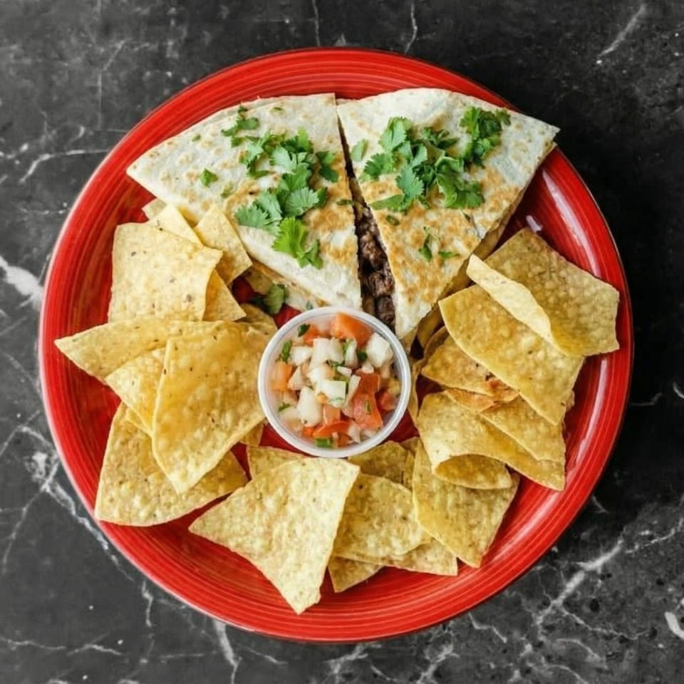 Two quesadilla halves topped with cilantro, surrounded by tortilla chips and a small cup of pico de gallo.