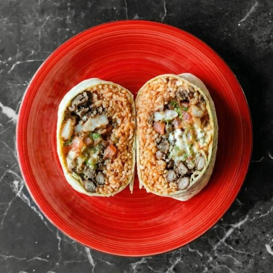 A large burrito, cut in half, revealing rice, beans, meat, and salsa on a red plate.